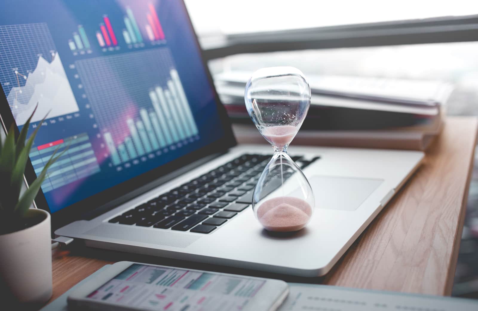 Business concepts with businessman holding hourglass with graph chart on computer laptop