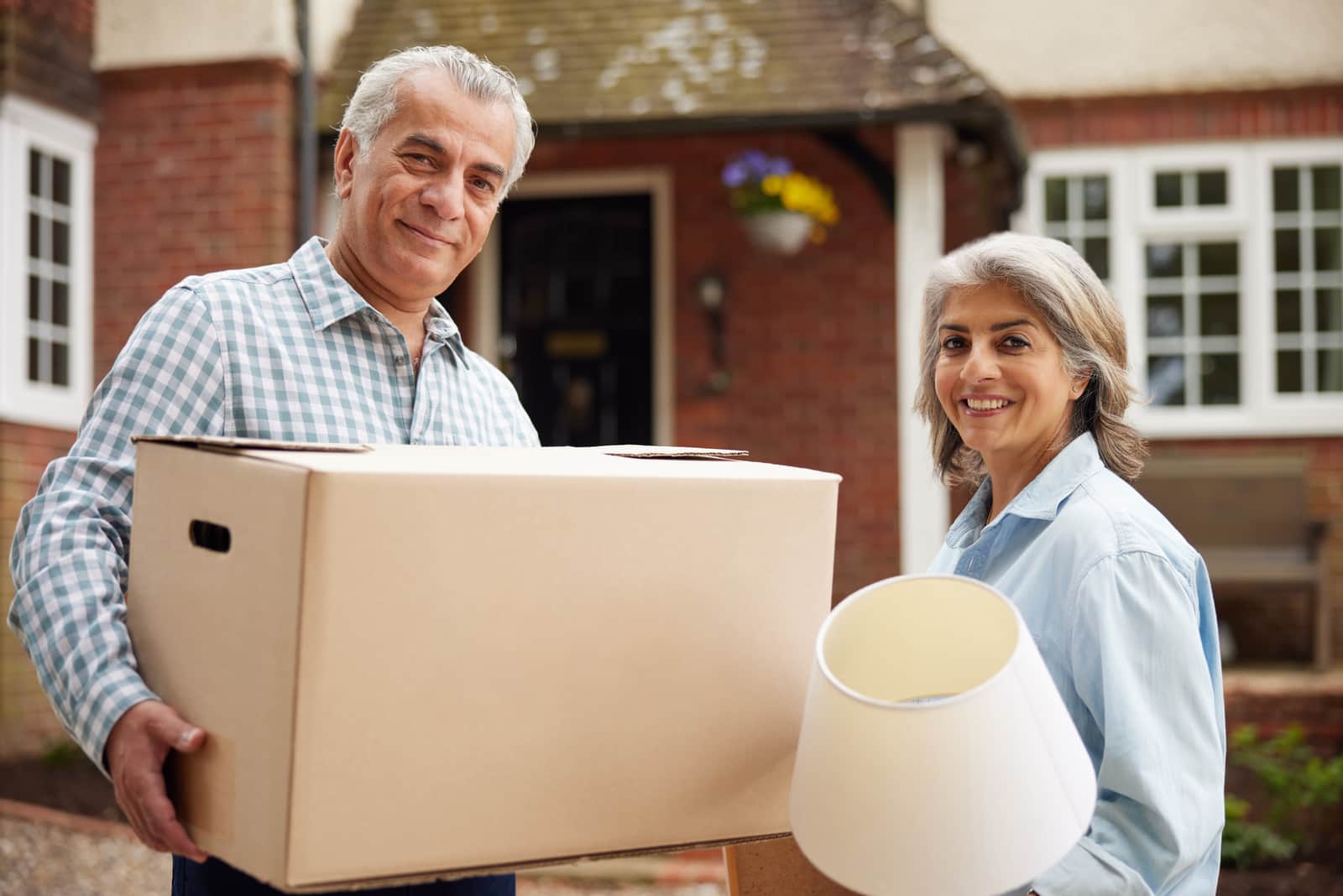 Mature Couple Carrying Boxes On Moving Day In Front Of Dream Home