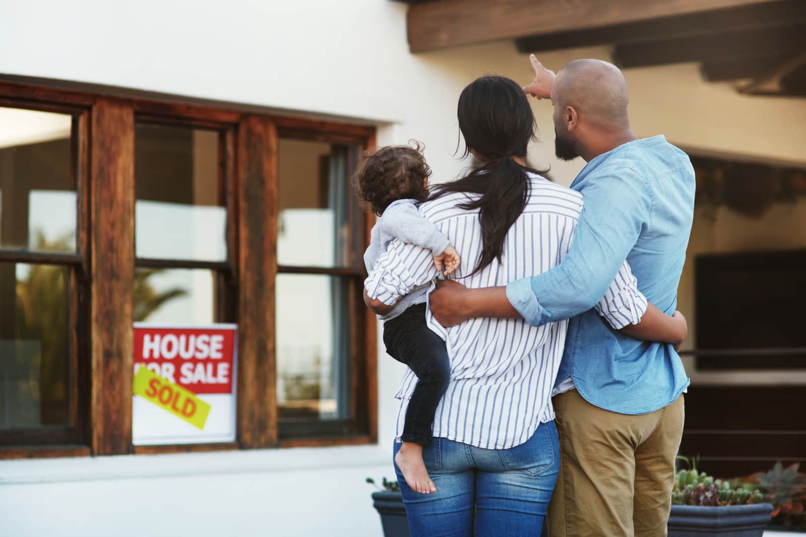 family standing in front of house with a sold sign in the window