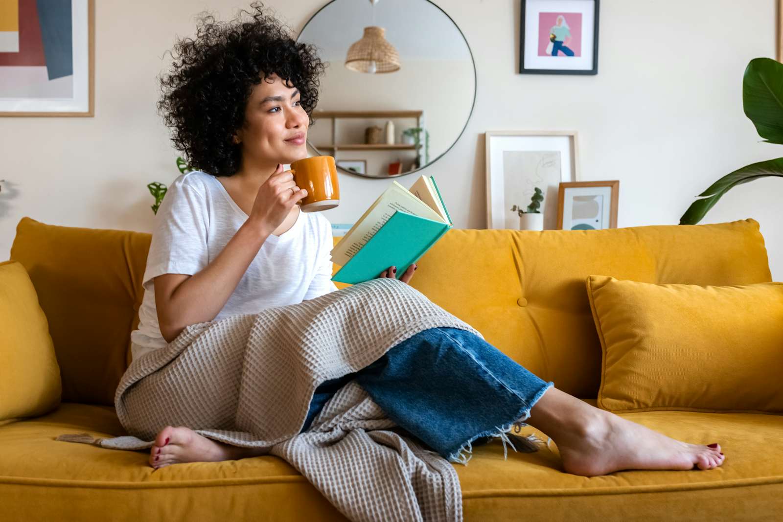 Woman reading a book at home, drinking coffee sitting on the couch. Copy space.