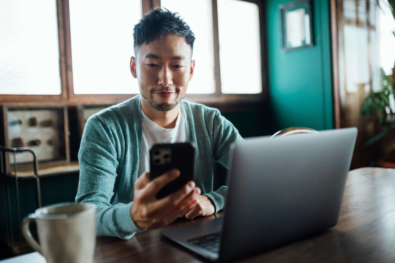 man looking at smartphone while working on laptop computer in home office