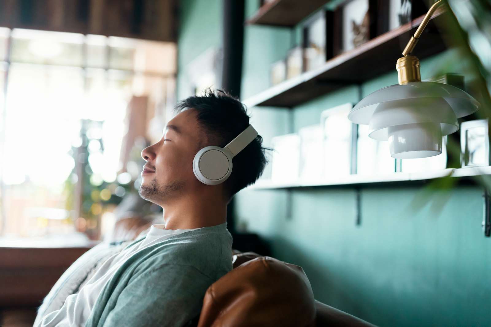 Young man with eyes closed, enjoying music over headphones while relaxing on the sofa at home